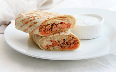 shawarma with chicken, vegetables on a white plate next to the sauce, light background