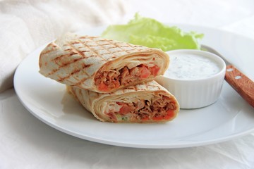 shawarma with chicken, vegetables and herbs on a white plate next to the sauce and knife on a light background