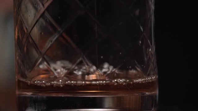 A bartender is pouring spirit and liquor into the stirring glass and start to stir along a lot of ice using a long copper bar spoon.