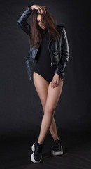 Fototapeta na wymiar Brunette girl in a black leather jacket . Beautiful model on a dark background. Full-length studio photosession