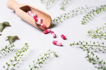 Scoop with pills and herbs on light background