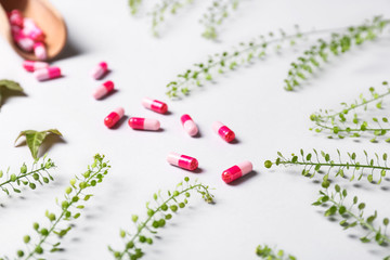 Pills with herbs on light background