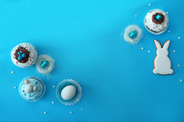 Tasty Easter cupcakes with sweets and egg on color background