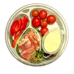 Healthy fast food in a transparent container. Vegetable salad for quick cooking with tomatoes, bell peppers, jamon and lettuce. On gray background. Top view. Isolated.