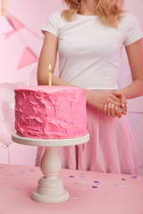 cropped view of woman standing near baked tasty birthday cake with burning candle on cake stand