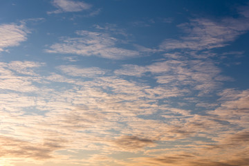 Horizontal photo of winter evening blue sky background with white and yellow layered clouds on warm sunset