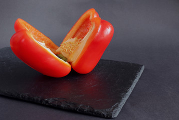 The red, sweet Bulgarian pepper is cut in half and lies on a black dish