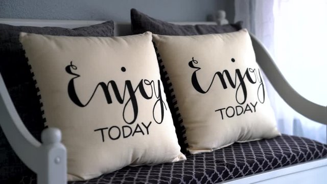 "Enjoy today" pillow being set down on a nice bench in a room