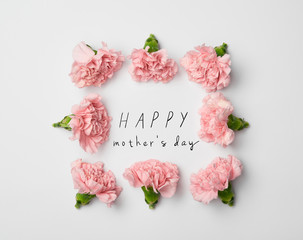 top view of floral frame made of pink carnations on white background with happy mothers day...