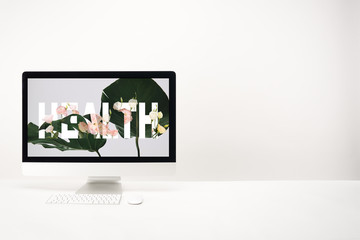 computer with health lettering and green monstera leaves on monitor on white background