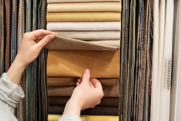 Young woman choosing fabric for new curtains in shop