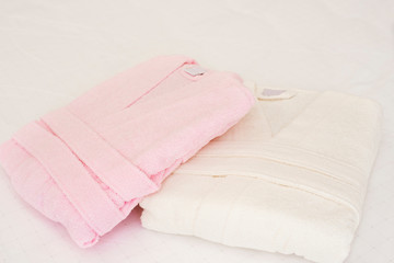 Folded bathrobe on bed in room. White and pink, two robes