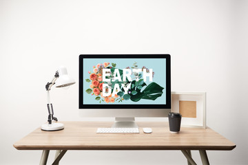 computer with green monstera leaves and flowers and earth day lettering on monitor on wooden desk