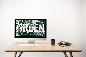 computer with green leaves and green lettering on monitor on wooden desk