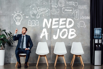 businessman in suit showing idea gesture and sitting in waiting hall with need a job lettering on wall