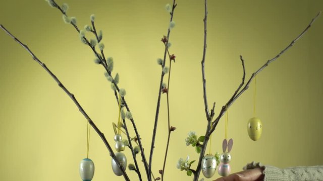 Weidenk&auml;tzchen &Auml;ste und Apfelbaum &Auml;ste in einer Glasvase. Die Apfelbl&uuml;te hat begonnen. Die &Auml;ste werden von einer Frauenhand mit Osterhasen und Ostereiern dekoriert.