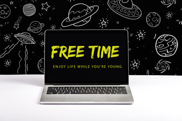 laptop on table with enjoy life while you are young and free time lettering on screen with white galaxy illustration on black