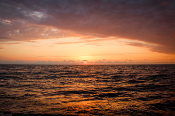 Golden, Fiery sunset on the Black Sea, on the beach. Coast, stones, waves, sun, beautiful sky, clouds. August, Batumi, Georgia. Water, lightness, play. Pink, lilac, crimson