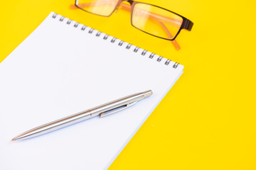 Glasses, notepad and pen on a yellow background