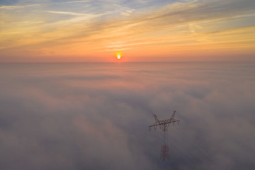 Foggy power lines sunrise morning with beautiful colours. Clouds and  supporting structure with natural colors.