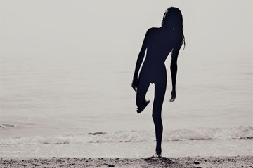 Silhouette of a skinny young girl walking along the beach