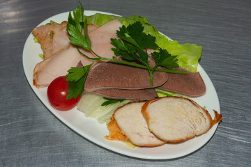 Food served on board for crew members of the airplane. Beef tongue, boiled pork, ham, parsley, cherry tomato. Close up. Selective focus.