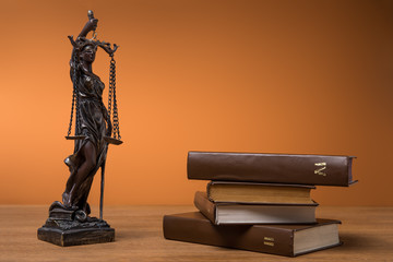 bronze statuette with scales of justice and volumes of brown books on table