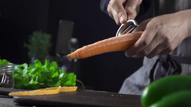 Cook cleans orandge carrot in the kitchen slow motion