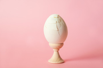 A cracked egg on a pink background close-up and copy space. One egg, easter concept, smash