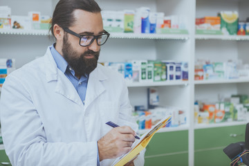 Cropped shot of a bearded mature pharmacist looking concentrated, filling medical papers while working at his drugstore, copy space. Male chemist doing paperwork at the pharmacy, copy space