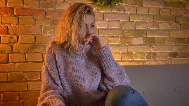 Closeup shoot of adult caucasian blonde female watching TV being touched and sad crying while sitting on the couch indoors at cozy home