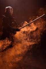 Kendo fighter in armor practicing with bamboo sword in smoke