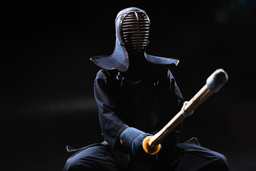 Kendo fighter in helmet holding bamboo sword on black