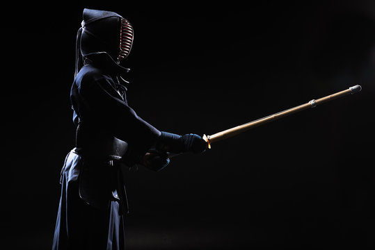 Kendo fighter in helmet holding bamboo sword on black