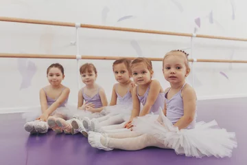 Plexiglas schilderij Dansschool Mooie kleine meisjes die naar de camera kijken, zittend op de vloer op balletschool. Schattige kleine ballerina& 39 s rusten na het sporten. Groep kleine meisjesdansers die maillots dragen die na ballet ontspannen  © mad_production
