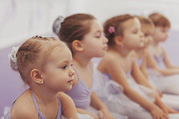 Close up of a beautiful little ballerina girl sitting with her classmates at ballet school. Group...