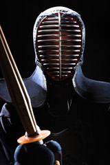 Kendo fighter in helmet holding bamboo sword isolated on black