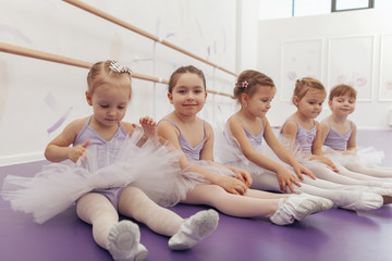 Group of cute little girls wearing ballet tutus sitting on the floor at dance studio. Adorable...