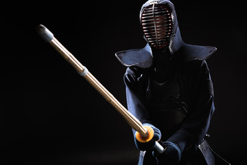Kendo fighter in armor practicing with bamboo sword on black