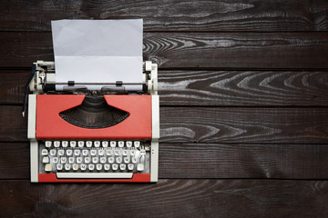red vintage typewriter with white blank paper sheet on dark wooden table