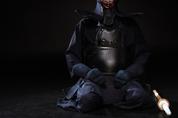 Partial view of kendo fighter in helmet with bamboo sword sitting on black