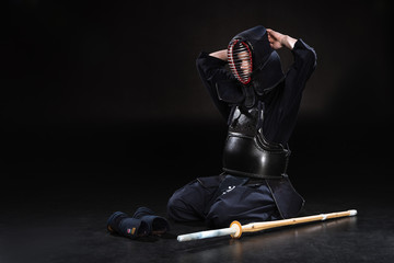 Kendo fighter sitting on floor and taking off helmet on black