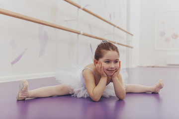 CUte happy little ballerina doing splits at dance school. Adorable little girl dreaming of becoming ballerina, exercising at ballet studio, copy space. Flexibility, gymnastics, health concept