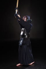 Full length view of kendo fighter in armor practicing with bamboo sword on black