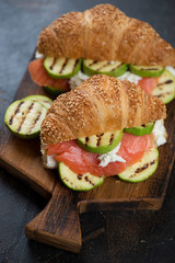 Croissants with red fish, ricotta cheese and grilled zucchini on a wooden serving board, studio shot