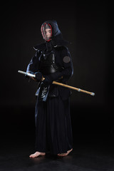 Naklejka premium Full length view of kendo fighter in helmet holding bamboo sword on black