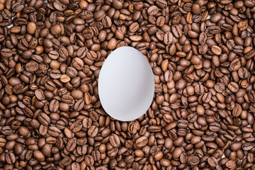 White egg on the freshly roasted coffee beans  background. Creative easter concept.