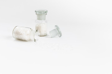 Obraz na płótnie Canvas Pure Natural Coarse Sea Salt Spilling Out of A Vial On White Background, Space For Text