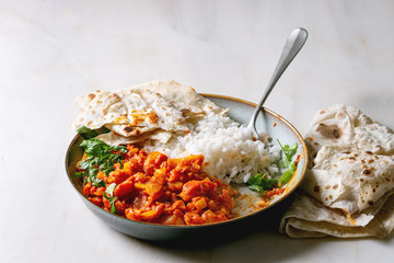 Started eaten Vegan vegetarian curry with ripe yellow jackfruit served in ceramic bowl with rice, coriander and homemade flatbread flapjack over white marble table.