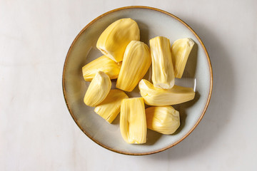 Ripe raw peeled jackfruit in ceramic plate over white marble background. Flat lay, space